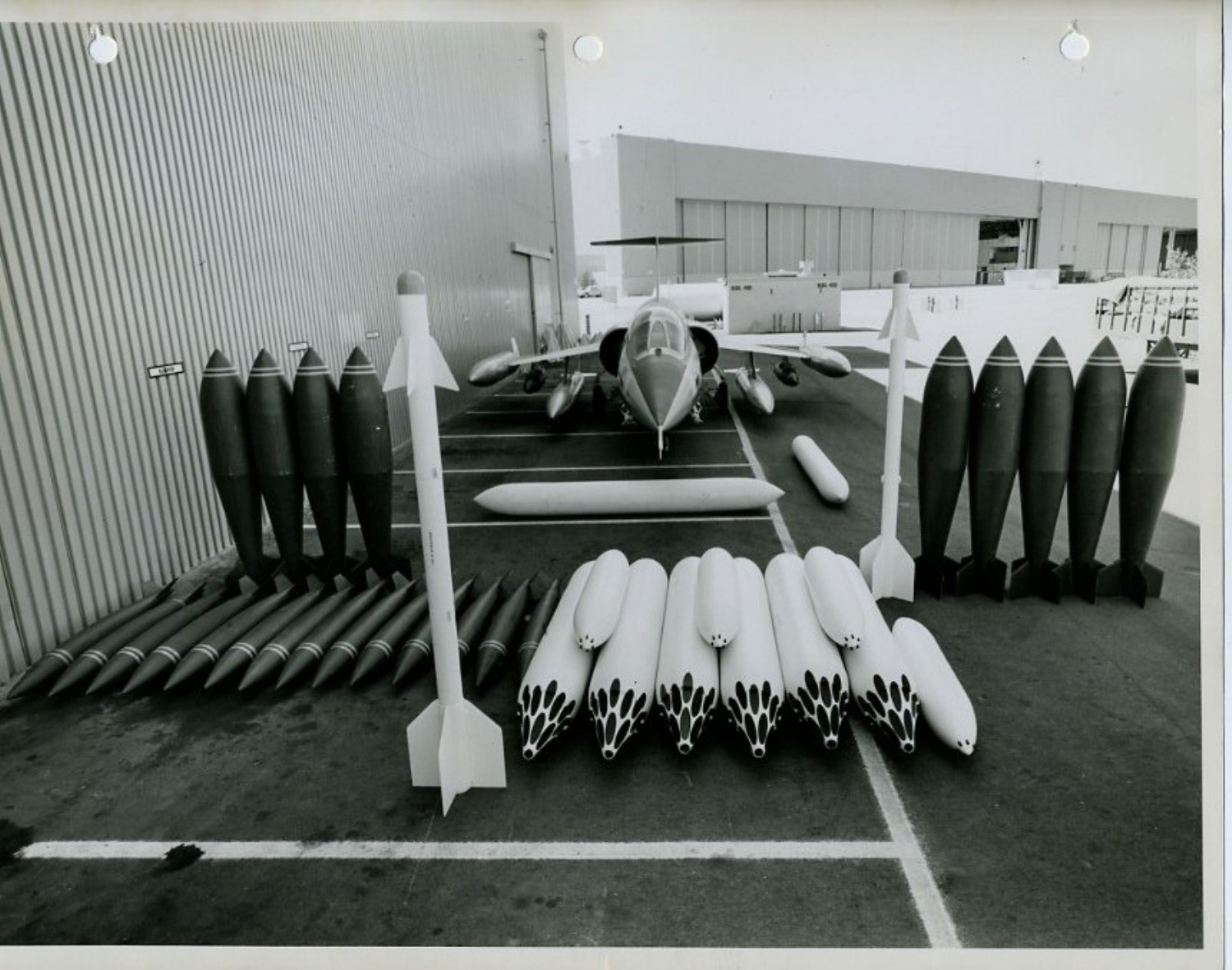 Lockheed-Aufstellung mit Bomben, Raketenbehältern und weiteren Waffen vor einem am Boden abgestellten Starfighter.
