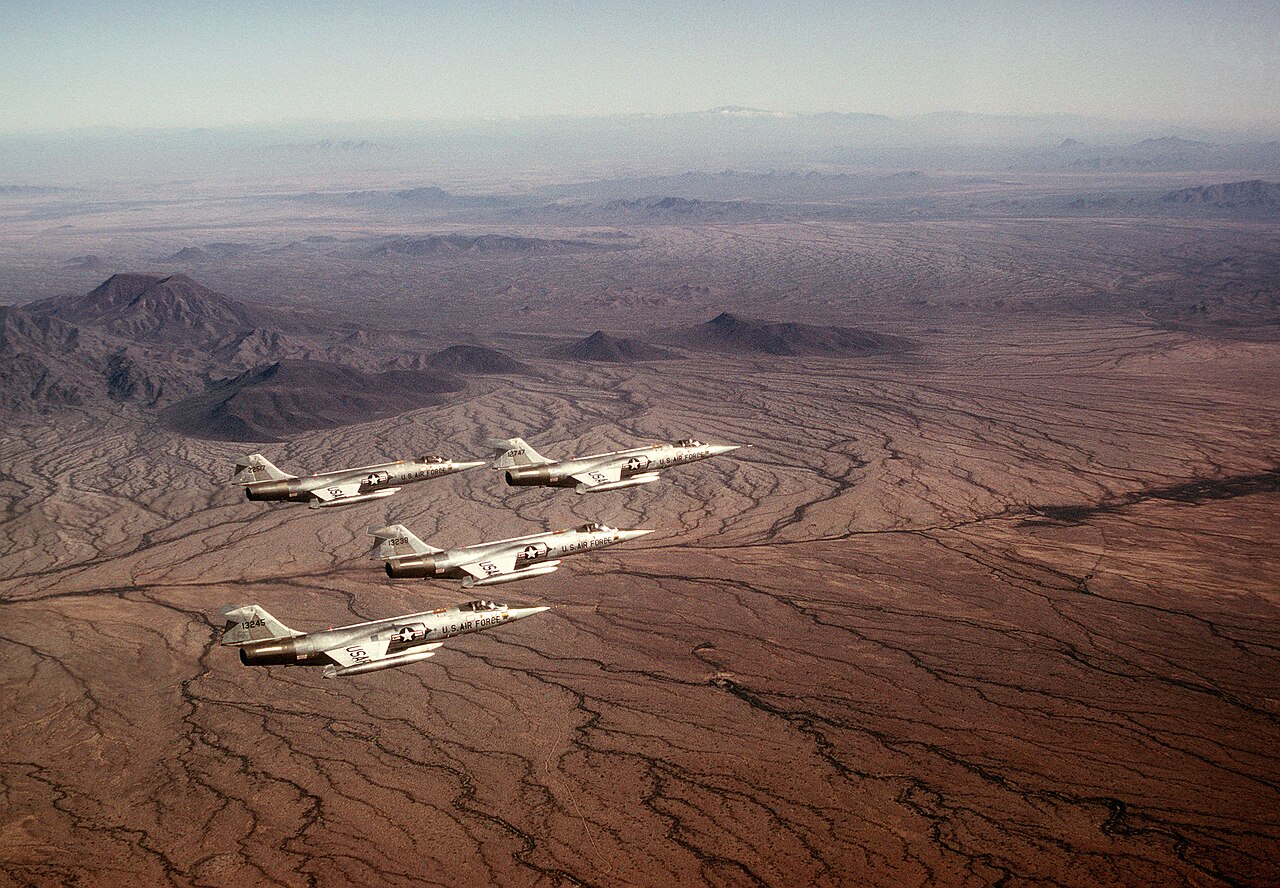 Vier F-104G mit US-Air-Force-Kennzeichen fliegen in Formation über der Wüstenlandschaft Arizonas.